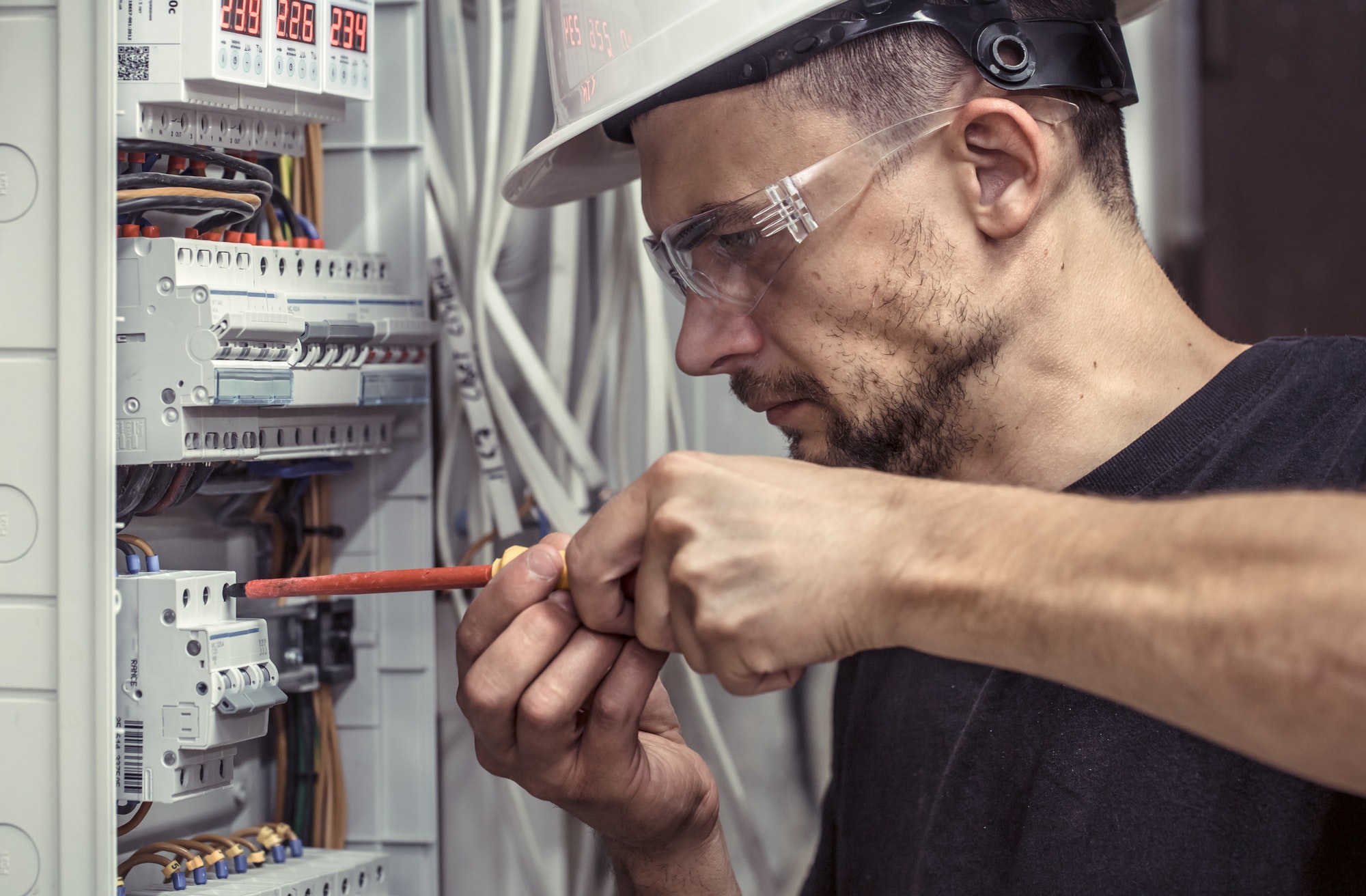 a male electrician works in a switchboard with an electrical connecting cable 24/7 Electrical - Your Local Trusted Electricians